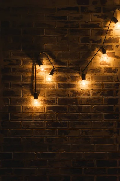 Brick wall texture. The interior of the room. Finishing material. Repair of premises. Brick wall in the interior. Lights on the wire hanging on the wall. The lights in a dark room.