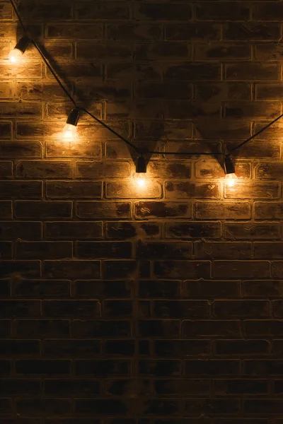 Brick wall texture. The interior of the room. Finishing material. Repair of premises. Brick wall in the interior. Lights on the wire hanging on the wall. The lights in a dark room.