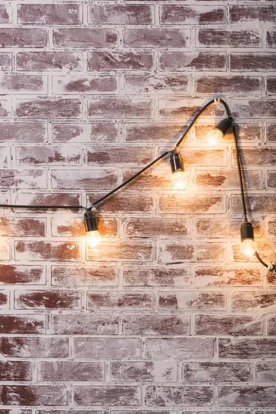 Brick wall texture. The interior of the room. Imitation of masonry. Finishing material. Repair of premises. Brick wall in the interior. Lights on the wire hanging on the wall. Lights on.