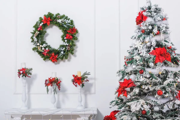 赤と銀の丸いおもちゃ 光る花輪 ポインセチアの花で飾られたクリスマスツリー 白い見掛け倒しの羽 松葉の枝で飾られたキャンドル 壁にクリスマスリース — ストック写真