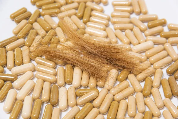 Pills and hair on a white background. Vegetable vegan capsules. Biologically active additives. Means for improving hair growth. Dietary supplement. Hair loss