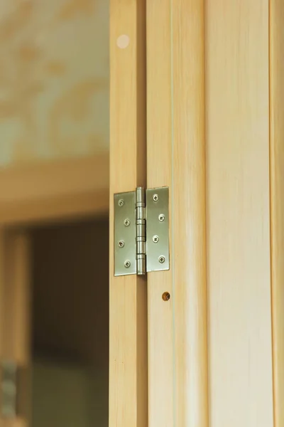 Interior wooden door of light color. Metal door mounting. Wood surface texture. Metal door hinge.