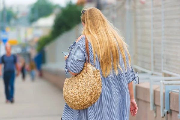 Girl with a wicker round bag walking around the city. A woman with white hair in the shirt on the background of the city. Walk on the street.