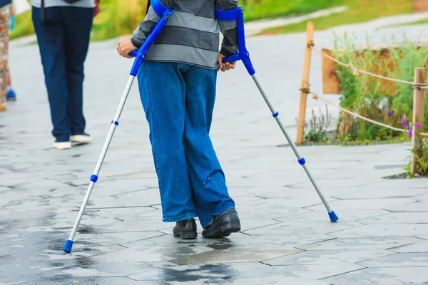 古いおじいちゃんは 松葉杖で歩いています 無効になっている男は街を歩きます 金属の松葉杖が青い — ストック写真