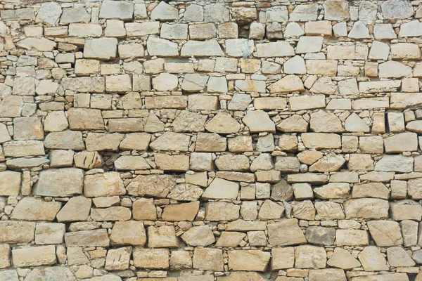 The texture of an old stone wall. Green grass grows on the background of the old building. Cracks and chips on the brick wall.