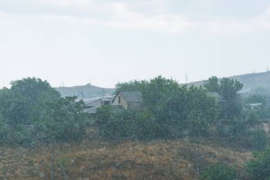 Engebeli arazi. Bir arka plan yeşil ağaç evler. Tepeler yeşil bitki örtüsü ile. Köyün üzerinde bulutlu gökyüzü.