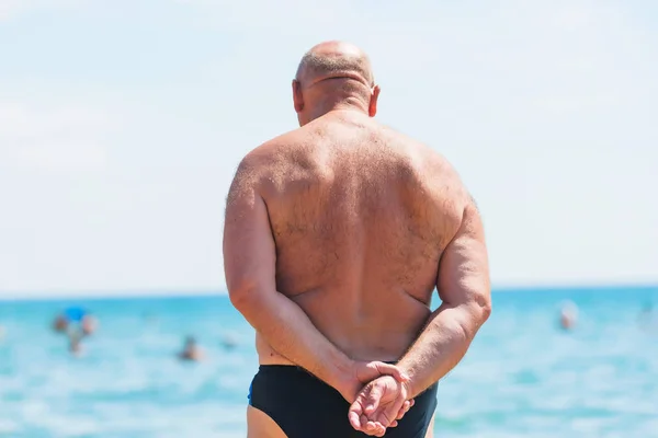 A man in black swimming trunks standing on the beach. Black Sea. Rest in Crimea. People swim in the sea.
