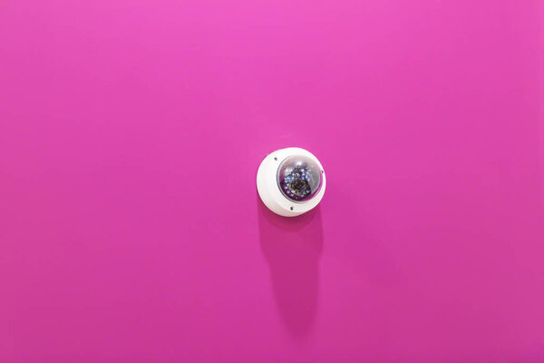 Round white surveillance camera on pink wall background. the interior of the room. The wall is painted pink.