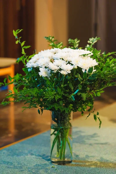 A bouquet of white flowers is on the table. Decoration of the interior of the room with fresh flowers. White flowers in a glass vase.