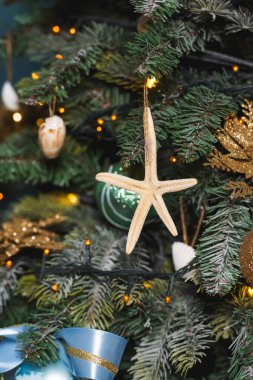 Altın ve mavi renklerde Noel dekorasyonu. Deniz tarzında yeni yıl dekorasyon. Mavi arka planda Noel ağacının tasarımında deniz kabuğu, denizatı ve yıldızlar. Yılbaşı ağacında yıldız balığı, şeritler ve topları.