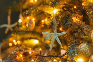 Altın ve mavi renklerde Noel dekorasyonu. Deniz tarzında yeni yıl dekorasyon. Mavi arka planda Noel ağacının tasarımında deniz kabuğu, denizatı ve yıldızlar. Yılbaşı ağacında yıldız balığı, şeritler ve topları.