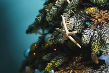 Altın ve mavi renklerde Noel dekorasyonu. Deniz tarzında yeni yıl dekorasyon. Mavi arka planda Noel ağacının tasarımında deniz kabuğu, denizatı ve yıldızlar. Yılbaşı ağacında yıldız balığı, şeritler ve topları.