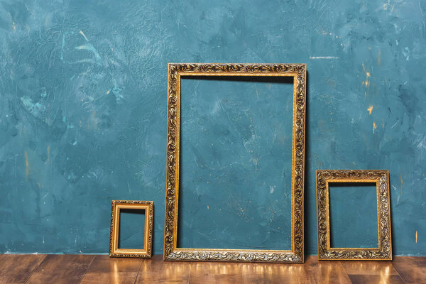 Gold large frame on a blue wall background. Decorative element. Vintage gold plated picture frame. Vintage photo zone.