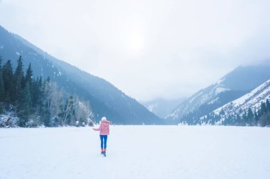 Kazakistan'ın Lake Kolsay. Donmuş göl üzerinde kız. Kazakistan Cumhuriyeti Kış Turizm. Kadın pembe kış ceket.