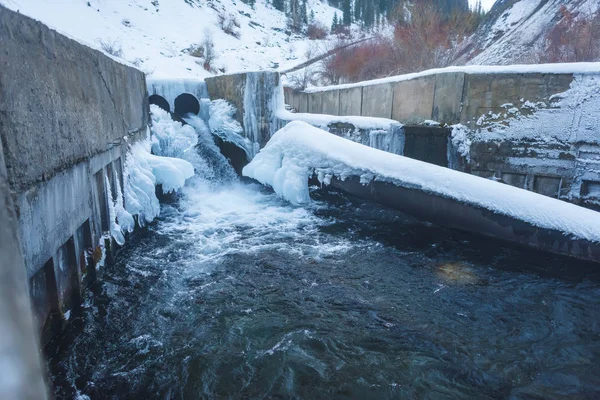 Frozen water channel. Mountain river in winter. Icing on the bank of the stream. Bypass channel. Head of river water from the pipe.