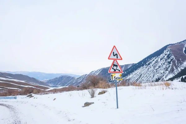 Road sign Slippery road in the mountains. Sign Dangerous turns on a winter road. Snow mountain road. The length of the zone of the mark is five kilometers.
