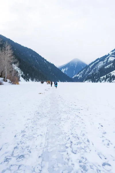 Ice-covered lake in the mountains. People on ice lake in winter. Lake Kolsay in Kazakhstan. Winter tourism in the Republic of Kazakhstan.