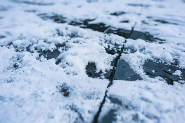 Frozen water surface. Ice on a mountain lake. Cracked on ice. Cracked on the surface of a frozen lake. Snow on ice. Air bubbles in the ice. The texture of the frozen surface of the water.