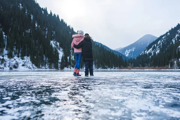 Ice-covered lake in the mountains. Couple on ice lake in winter. Lake Kolsay in Kazakhstan. Winter tourism in the Republic of Kazakhstan.