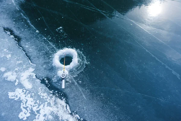 Ice fishing on a mountain lake. Fishing on the frozen surface of the lake. Equipment for ice fishing. Hole with fishing rod on the ice.