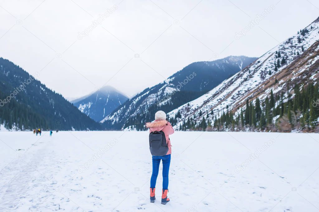 Mountain ice-covered lake in the mountains. Girl on the lake in winter. Lake Kolsay in Kazakhstan. Winter tourism in the Republic of Kazakhstan.