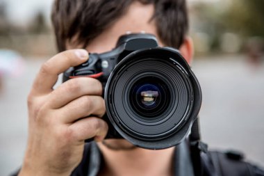 Bir fotoğraf makinesi olan bir adam. Fotoğrafçı yüz yakınındaki bir kamera ile. Adam sokakta fotoğraf çekmek. Kamera tarafından kaplı yüz.