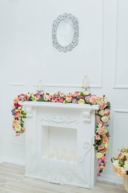 Şömine çiçekler ile dekore edilmiştir. Dekoratif alçı. Beyaz duvar. Metal mum sahipleri mumlar. Bahar dekoru. Odanın iç mekanı. Dekoratif şömine.