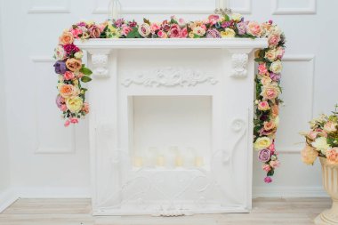 Şömine çiçekler ile dekore edilmiştir. Dekoratif alçı. Beyaz duvar. Metal mum sahipleri mumlar. Bahar dekoru. Odanın iç mekanı. Dekoratif şömine.