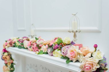 Şömine çiçekler ile dekore edilmiştir. Dekoratif alçı. Beyaz duvar. Metal mum sahipleri mumlar. Bahar dekoru. Odanın iç mekanı. Dekoratif şömine.