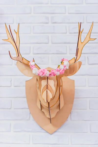 White brick wall. Wooden deer head. Wall decoration. Paper garland in the shape of hearts. Artificial flowers. Decorative element. The interior of the room.