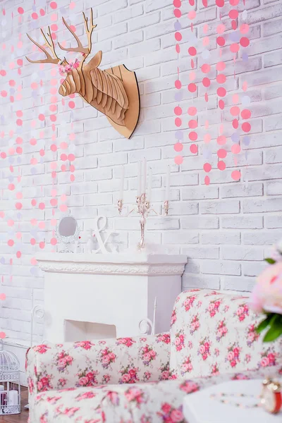 White brick wall. Wooden deer head. Wall decoration. Paper garland in the shape of hearts. Artificial flowers. Decorative element. The interior of the room.