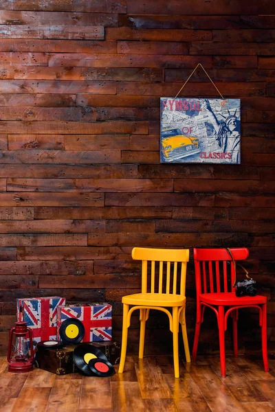 Wooden wall. The chairs are red and yellow. Vinyl record. Suitcases with British print. Photo zone. Oil lamp. Leather brown suitcase.