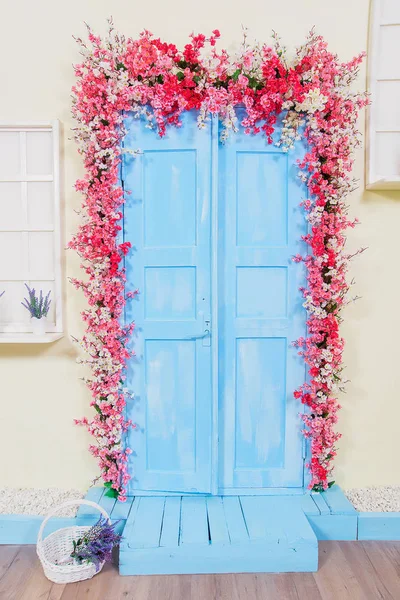Spring decor. Wooden doors painted in blue. Doors decorated with pink flowers. White wicker basket. Imitation of Windows. Lavender in pots.