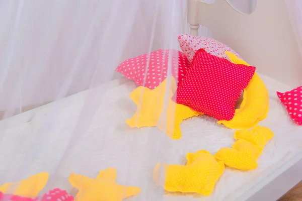 White brick wall. The interior of the children\'s room. Four-poster bed. Pink square pillows. The texture of the fabric. Decorative element. Yellow pillows in the shape of a star and a heart.