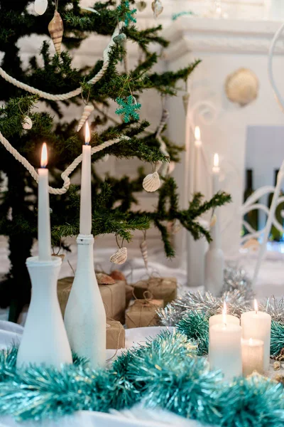 Christmas decor. White candle. Green and silver tinsel. Decorative sea shells. Packed gifts. Christmas tree.