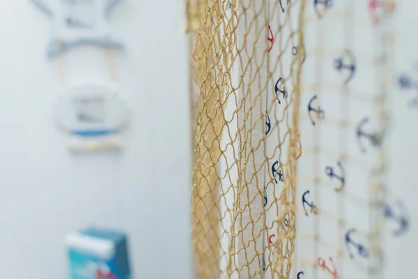 Interior decor in the marine style. Fishing net on the background of bright walls. Decorative blue ship anchor.