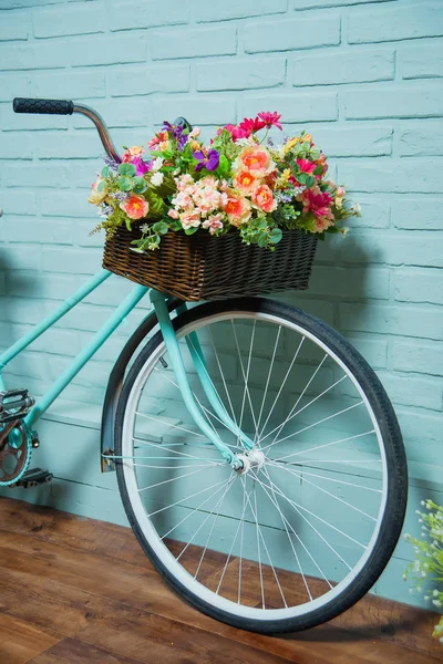 Bicycle with a basket of flowers. Blue brick wall. Summer decor. Decorative brickwork. Wicker basket with flowers.