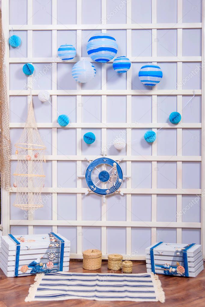 The interior of the room. Decor in marine style. Shelves of wooden boxes. Photo zone. Wooden shutter. Decorative life buoy. Photo zone. Sea shell. Toy in the form of a ship's anchor.