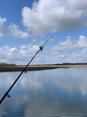Sabah SYR Darya nehrinin kıyısında. Suyun yüzeyinin dokusu. Nehrin üzerinde bulutlu gökyüzü. Arka planda balıkçılık çubuğu .