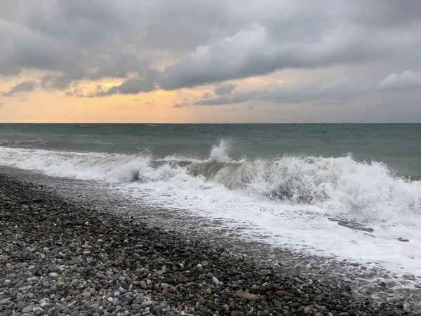 Sunset in a cloudy sky on the sea. Big wave. Rest on black sea. Rocky beach of Batumi.