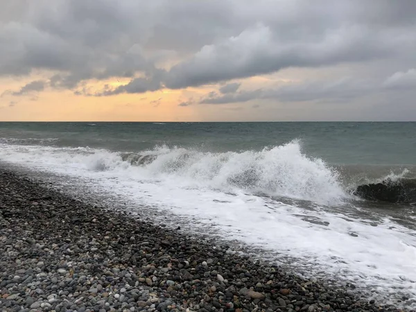 Sunset in a cloudy sky on the sea. Big wave. Rest on black sea. Rocky beach of Batumi.