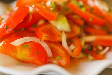 Beyaz tabakta domates ve soğan salatası. Otlarla sebze salatası. Kırmızı domates. Masadaki çanak.