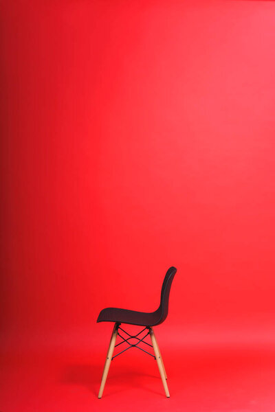 Black chair on a red background. Studio paper background. Designer chair with a plastic back and wooden legs.