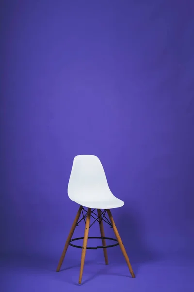 White chair on a purple background. Studio paper background. Design bar stool with plastic back and wooden legs.