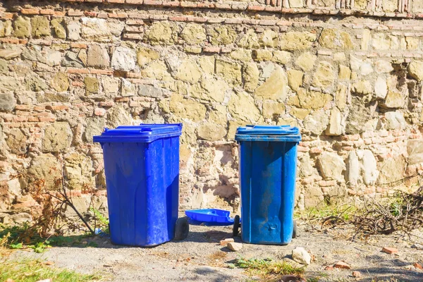 Blue garbage cans on the background of a stone building. Street containers for waste disposal. Old stone building. Architecture in Georgia..
