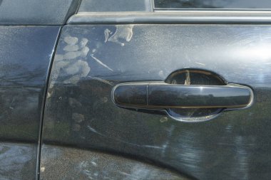 Siyah arabanın tozu. Araba kapı kolu. Arabanın metal gövdesinde çizikler var. Tozlu metal yüzey.