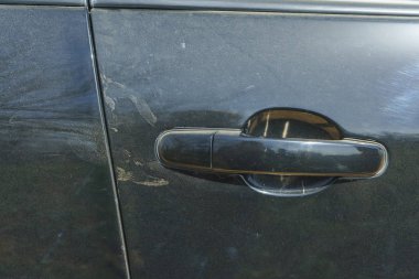 Siyah arabanın tozu. Araba kapı kolu. Arabanın metal gövdesinde çizikler var. Tozlu metal yüzey.