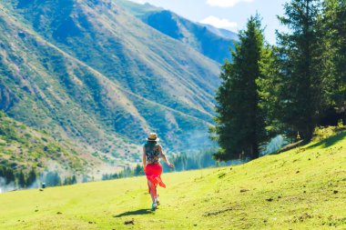 Dağlara karşı kırmızı etekli bir kız. Kırgızistan'da dinlenin. Dağ geçidi Jety Oğuz. Issyk-Kul Gölü bölgesinde doğa.