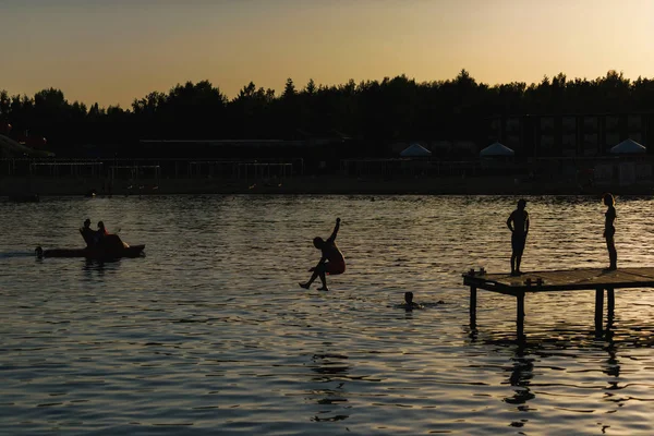 People jump from the pier into lake Issyk Kul. Guys swim in the lake at sunset. The texture of the surface of the water. Rest in Kyrgyzstan.