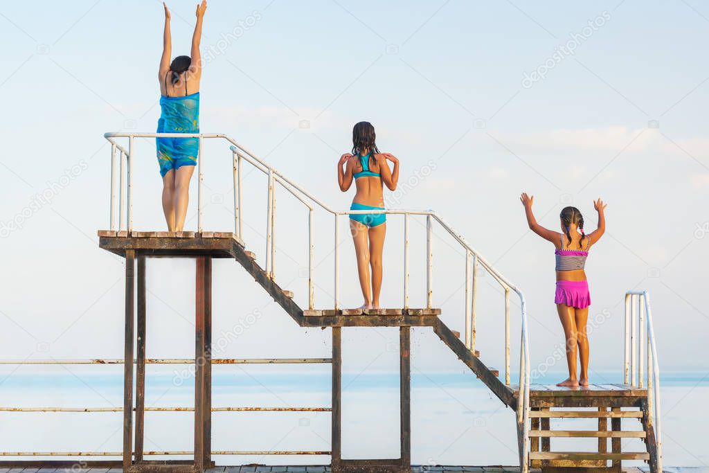 The girls are on a wooden pier.  Trip to Issyk Kul lake. Girls in colorful swimsuits. Rest in Kyrgyzstan.